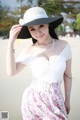 A woman in a white dress and a black hat on the beach.