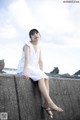 A woman in a white dress sitting on a concrete wall.