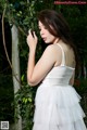 A woman in a white dress standing next to a tree.