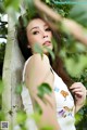 A woman leaning against a tree in a white dress.