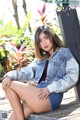 A woman sitting on a wooden bench wearing a denim jacket.