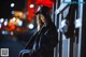 A woman in a black coat and hat leaning against a fence.