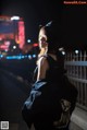 A woman standing on a bridge at night with a backpack.