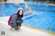 A woman crouching down next to a swimming pool.