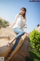 A woman sitting on a stone wall in a white sweater and jeans.