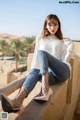 A woman sitting on a wall wearing a white sweater and jeans.