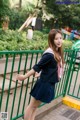 A woman in a school uniform leaning against a fence.