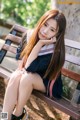 A woman sitting on a wooden bench with her legs crossed.