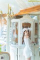 A woman in a white dress and hat standing in front of a cabinet.