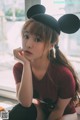 A woman wearing a mickey mouse hat sitting on a window sill.