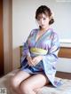 A woman in a blue kimono sitting on a bed.