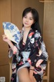 A woman in a kimono sitting on a chair holding a fan.