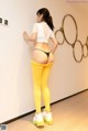 A woman in a white top and yellow leggings leaning against a wall.