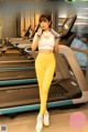 A woman in a white top and yellow leggings standing in front of a treadmill.