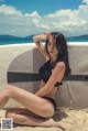 A woman in a black bikini sitting on a beach.