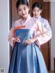 A woman in a blue and pink hanbok standing next to another woman.