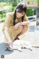 A woman in a yellow dress petting a white cat.