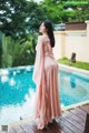 A woman in a pink dress standing by a swimming pool.