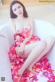 A woman sitting in a bathtub covered in rose petals.