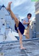 A woman in a school uniform doing a kick on a rooftop.