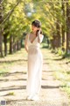 A woman in a white dress standing on a dirt road.