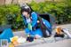 A woman in a blue dress sitting on the ground next to a trash can.