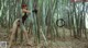 A woman in a black bathing suit holding a sword in a bamboo forest.