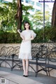 A woman in a white dress standing next to a bench.