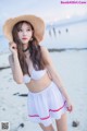 A woman in a white bikini and a straw hat on the beach.