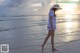 A woman in a white dress and hat walking on the beach.