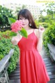 A woman in a red dress holding a pink flower.