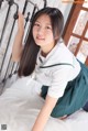 A woman in a school uniform is posing on a bed.