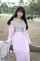 A woman in a pink dress sitting on a wooden fence.