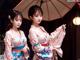 Two women in kimonos standing next to each other holding an umbrella.