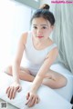 A woman in a white tank top sitting on a bed.