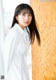 A woman in a white shirt leaning against a wooden wall.