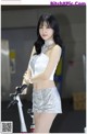 A woman in a white top and silver shorts standing next to a bike.