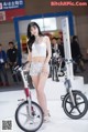 A woman standing next to a bike on display.