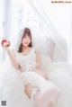 A woman in a wedding dress sitting on a bed holding a rose.