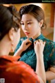 A woman putting on a green dress in front of a mirror.