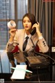 A woman in a business suit sitting at a desk talking on a phone.