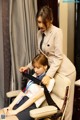 A woman in a suit and tie sitting on a chair next to a young girl.