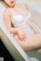 A woman in a white lingerie sitting in a bathtub.