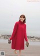 A woman in a red sweater dress walking on the beach.