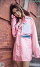 A woman leaning against a brick wall wearing a pink jacket.