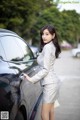 A woman standing next to a black car in a parking lot.