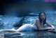 A woman in a white dress laying on a rock in the water.