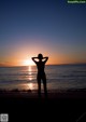 A silhouette of a woman standing on the beach at sunset.