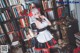 A woman dressed as a maid standing in front of a bookshelf.