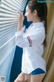 A woman in a white shirt and blue shorts leaning against a window.